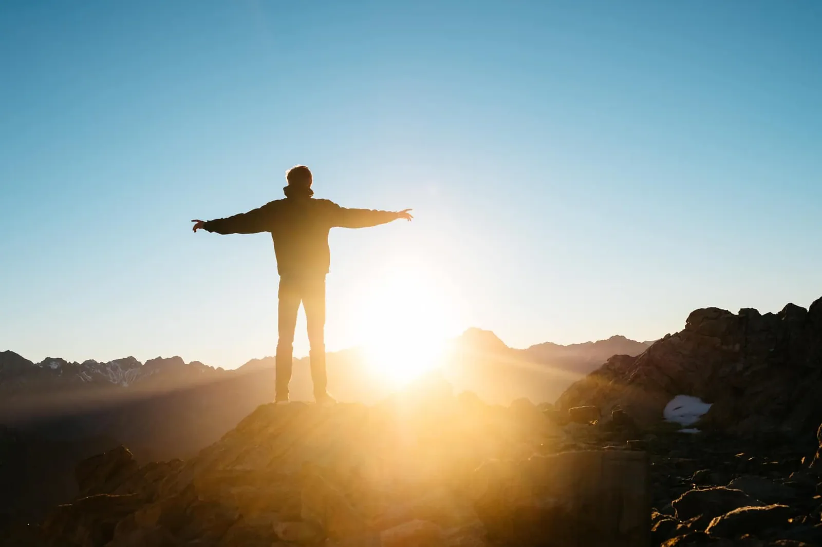 Ein Mann steht mit ausgebreiteten Armen auf einem Berggipfel.